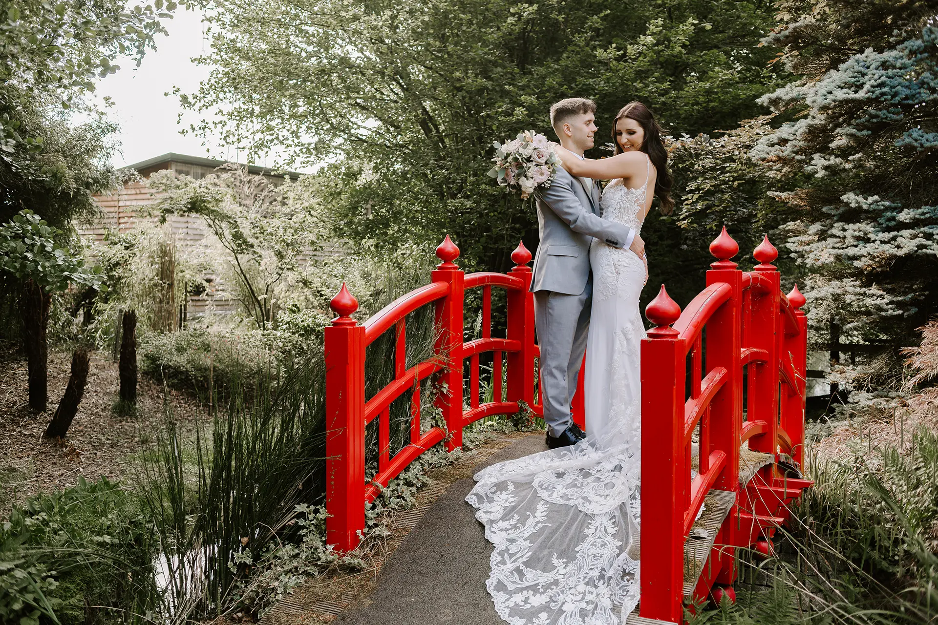 Couple posing for their wedding day photos on the signature red bridge in Rivervale Barn's gardens