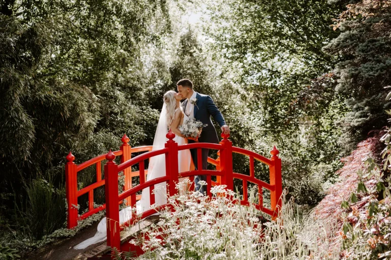 Couple kissing on the iconic red bridge in Rivervale Barn's gardens